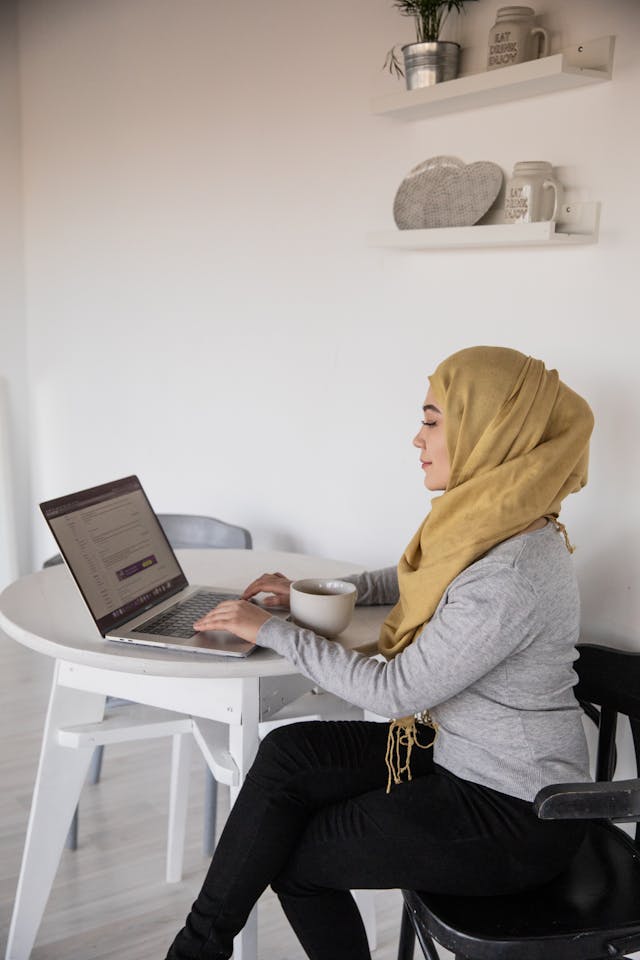 freelancer with hijab writing on her laptop with a cup of coffee on the table