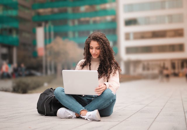 freelancer sitting on a roadside looking at her laptop