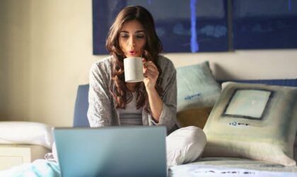 freelancer drinking coffee on the bed with open laptop