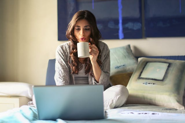 freelancer drinking coffee on the bed with open laptop