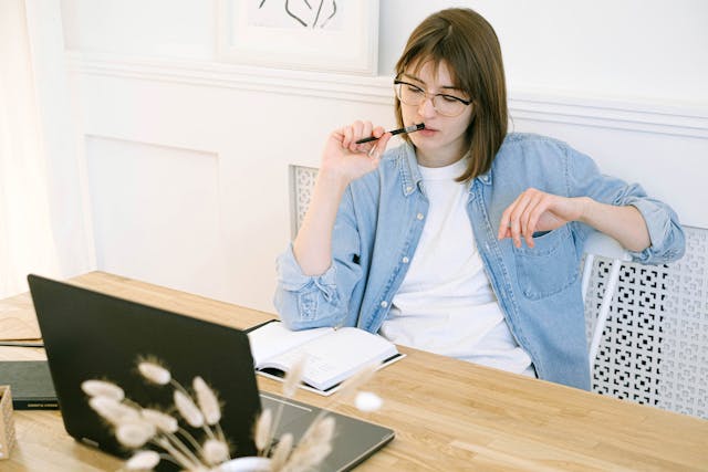 freelancer looking at her laptop with pen in her mouth